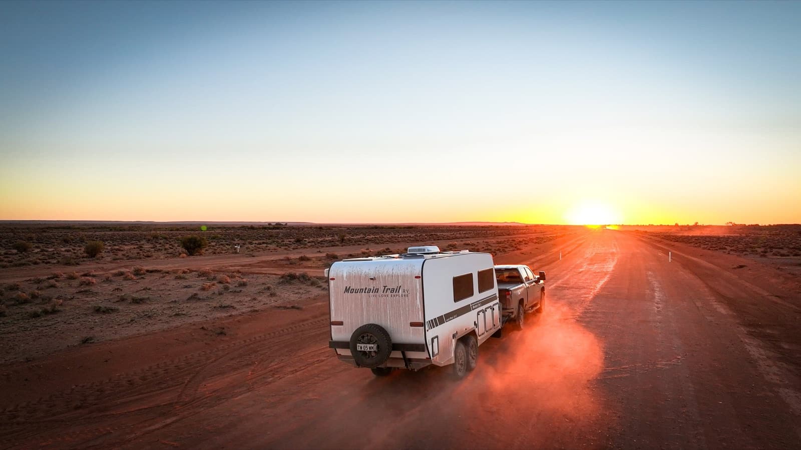 Caravan being towed into an outback sunset on a red dirt road in Australia
